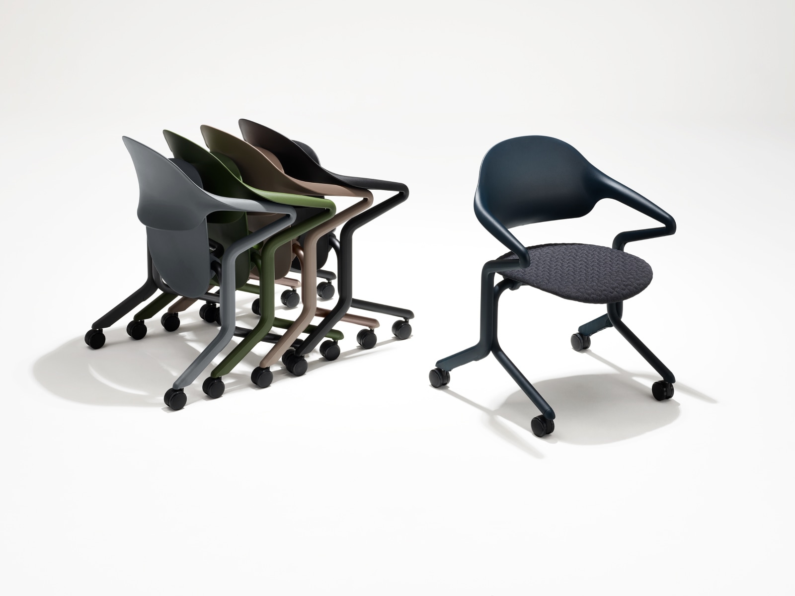 四把不同颜色和饰面的 Fuld 嵌套式座椅，嵌套摆放，旁边是一把 Fuld 嵌套式座椅，Nightfall，具有 3D 针织织物。